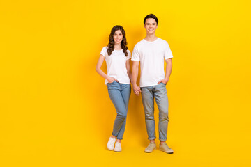 Wall Mural - Full length photo of charming sweet husband wife dressed white t-shirts holding hands arms empty space isolated yellow color background