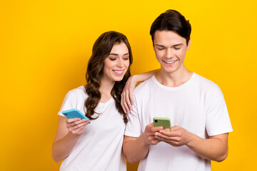 Canvas Print - Photo of two young people wear white t-shirt hold phone gadget chatting use apple device browsing app store eshop isolated on yellow color background