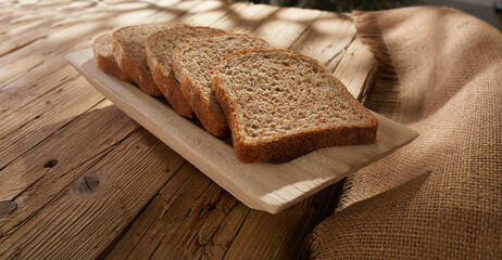 sliced bread on a wooden tray. breadboard on an old wooden table with cracks and rough fabric. baking in sun spots. rural lifestyle.