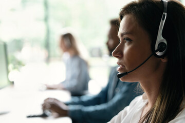 Canvas Print - Friendly smiling woman call center operator with headset using computer at office.