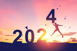 © tonktiti - Man jumping on sunset sky with birds flying at top of mountain and number 2024 abstract background. Happy new year and holiday concept.