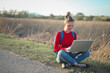 © olly - young woman backpacker sitting on the roadside uses a computer