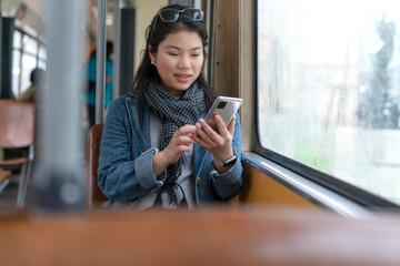 Young and happy asian female woman using smartphone while sitting near the window in the public transport shuttle bus during the trip while raining outside woman travel in Europe vacation