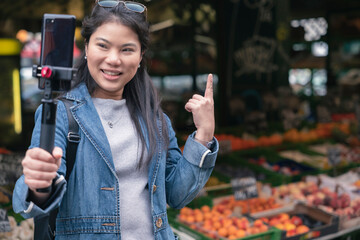 asian female blogger vlogger record vlog streaming video hold phone on selfie stick in open market urban city.Young Asian female tourist woman holding smartphone and recording videos travel concept