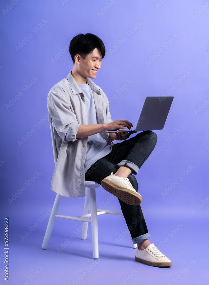full body image of young asian man using laptop on purple background ...