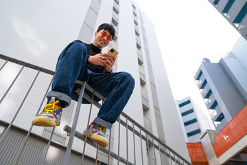 young asian man in red glasses walking happy using smartphone with futuristic modern building modern