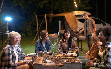 Group of friends having a meal and chatting happily at the campfire.