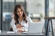 © crizzystudio - Asian businesswoman using a laptop to communicate Discuss and detail information about jobs online. Finance, accounting, income, and smiling happily at work.