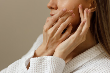 Acne skin of young woman in white bathrobe examines pimples on her face. Problematic skin on the face pustula. Portrait of girl removing pimples in the bathroom. Beauty and health of the skin close up