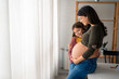 © Dorde - Young smiling little girl hugging pregnant mother, looking at her round belly, thinking about her baby brother or sister while standing near window with white curtains at home during the bright day.