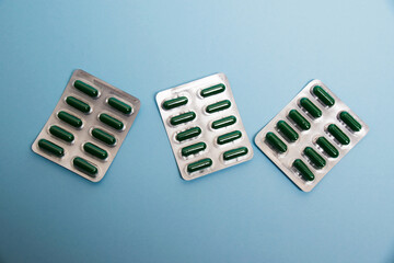 Wall Mural - Green capsules in a silver blister on a blue paper background, flatlay. Concept of immunity maintenance