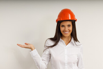 Beautiful model in orange construction helmet. Portrait of happy smiling brunette girl with long hair, dressed in white office shirt. Studio shot of young business woman on isolated white background.