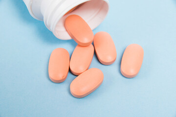 Wall Mural - White plastic jar with pink pills of vitamins for women on a blue background