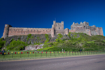 Wall Mural - Bamburgh Castle against a bright blue summer sky. Platinum Jubilee bunting decorating fence in foreground. Summer 2022 in Northumberland, UK