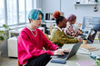 Diverse team of gen Z software developers working in office focus on Asian young man with colored hair using computer in foreground