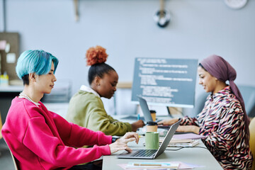 Side view portrait of Asian young man with colored hair using laptop in office, team in background