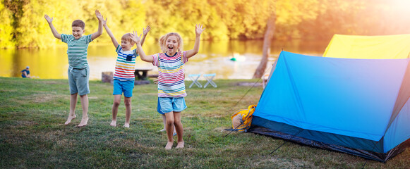 Wall Mural - Group of four children playing near colourful tents in nature.