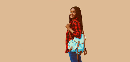 Wall Mural - Portrait of young african woman student with backpack on brown background