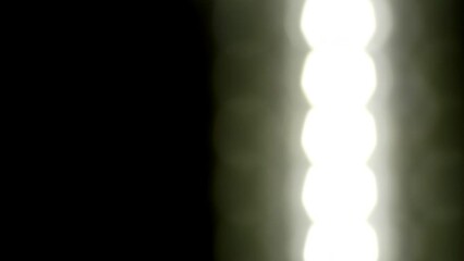 Wall Mural - White glowing blur circles fall down on black background. Loop 4K video. Falling bokeh lights in rows. Falling bokeh lights in rows. Glowing blurred bokeh circles in retro style.