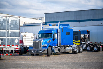 Cluster of big rigs semi trucks tractors and semi trailers standing on the warehouse parking lot in industrial park area