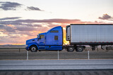 Fototapeta Kawa jest smaczna - Side view of the blue classic bonnet big rig semi truck with extended cab transporting cargo in refrigerated semi trailer driving on the highway road at sunset twilight