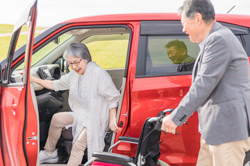 Wall Mural - 自動車から降りて車椅子に乗る高齢者女性と介助する男性（移乗）
