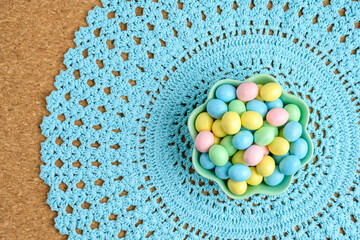 Wall Mural - Bowl of candy coated easter eggs on a pastel blue lace placemat
