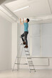 © New Africa - Young man installing ceiling lamp on stepladder indoors