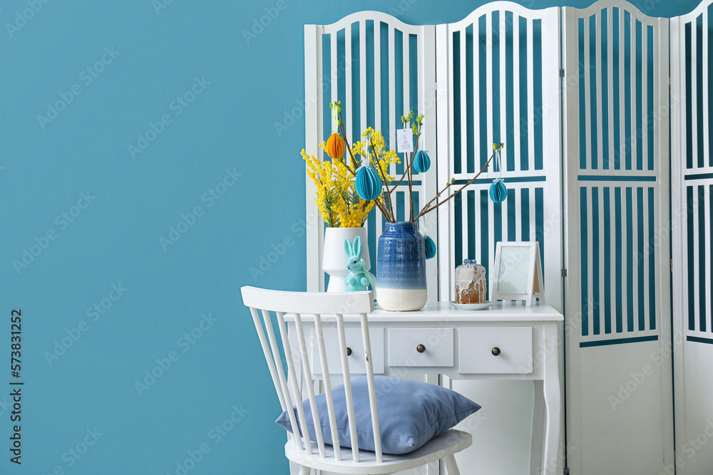Table with beautiful Easter decor, cake, mimosa flowers and folding screen near color wall