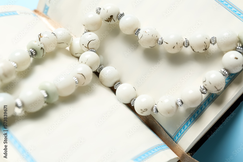Open Koran with prayer beads for Ramadan on blue background, closeup