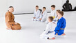 Group of little boys, children in kimono sitting on floor around coach. Children training indoors. Judo, jiu-jitsu training. Concept of martial arts, combat sport, sport education, childhood,
