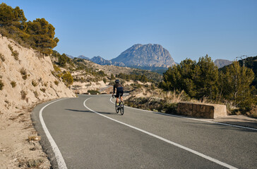 A cyclist riding on an empty road with mountains in the background.Male cyclist training on a gravel bike on the road.Inspiring photo of cycling sport.Athletic and fit athlete enjoy landscape mountain