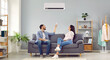 © Studio Romantic - Young happy man and woman turning on air conditioner sitting on sofa at home. Smiling couple of homeowners enjoying cool conditioned air using remote resting on couch together in living room. Banner.