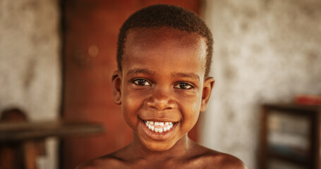Wall Mural - Close up portrait of a Cute Little African Kid with a Big Beautiful Smile Looking at the Camera. Happy Male Child in a Rural Area Representing Innocence, Peace and Hope. Documentary Footage
