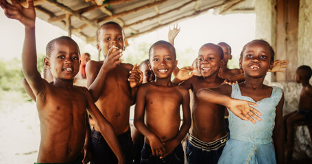 Wall Mural - A Group Of African Children, Laughing, Jumping And Waving in Rural Area. Black Kids Celebrating Life with Joy. Camera Captures Beauty and Essence Of Childhood, Innocence and Purity of Live in Village