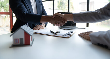 Wall Mural - Two young Asian businessmen shake hands after signing a contract to invest in a village project. real estate, with businesswomen joining in showing joy and clapping in the office.