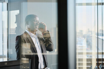 Poster - Happy mature director of business company in elegant suit talking to partners on smartphone while standing by workplace in office