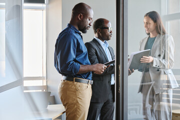 Poster - Mature director of business company talking to his secretary while male employee reading document and preparing for report