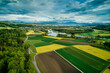 Blick über den Flachsee (Reuss). Ein buntes Mosaik. an Rapsfeldern, Ackerflächen und grünen Wiesen ziehen sich hin zu den Voralpen und Bergen am Horizont.