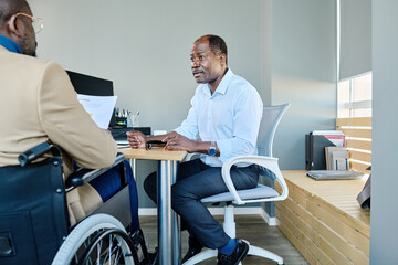 Poster - Mature director of broker corporation sitting by workplace in front of male subordinate with disability making him financial report at meeting
