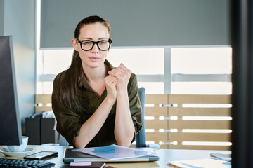 Poster - Young confident female boss or administrator of business company in eyeglasses and smart casualwear sitting by her workplace