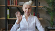 © RZ Images - Confident elderly woman teacher in white shirt making video call, online talking to webcam at classroom