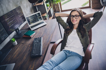 Wall Mural - Photo of dreamy happy lady programmer wear eyeglasses enjoying working pause arms hands behind head indoors workplace workstation