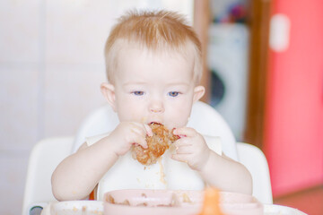 Happy childhood and delicious food. Funny child gets dirty with food. Little cute kid eats with his hands. Grimaces of a cheery baby. Close-up of a child's face