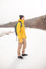 Wall Mural - The man dresssed yellow warm jacket and trousers, bagpack traveling in the snow landscape