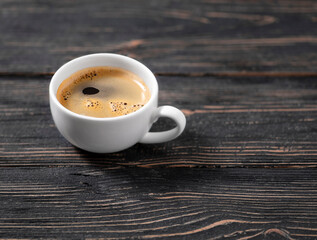 Coffee in a white cup stands on a dark wooden background