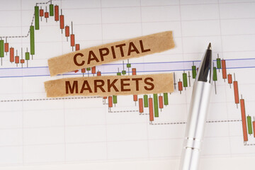On the chart of business quotes lies a pen and torn paper with the inscription - CAPITAL MARKETS