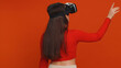 © Andrii Iemelianenko - Woman using headset helmet to play simulation game app online. Watching virtual reality 3D 360 video content. Girl in VR goggles isolated on studio red background. Futuristic technology. Rear view