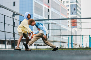 Wall Mural - Two adolescent intercultural schoolboys in activewear playing basketball on playground while trying to hold the ball during sports game