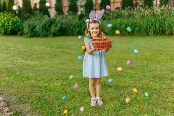 Wall Mural - a happy girl sprinkles eggs on the lawn with a fountain, for Easter hunting